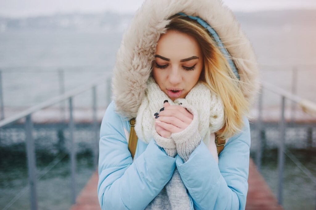 žena v modrej bunde s blond vlasmi si fúka na ruky pretože jej je zima